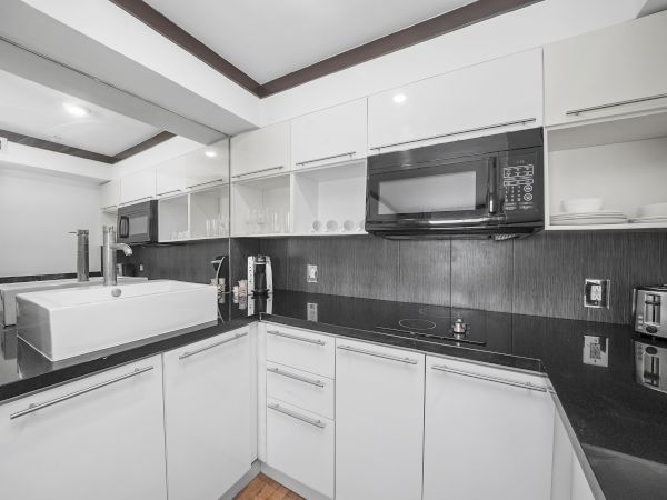 A modern L-shaped white kitchen with black countertops, upper cabinets, built-in microwave, and small appliances on the counter, clean and sleek.