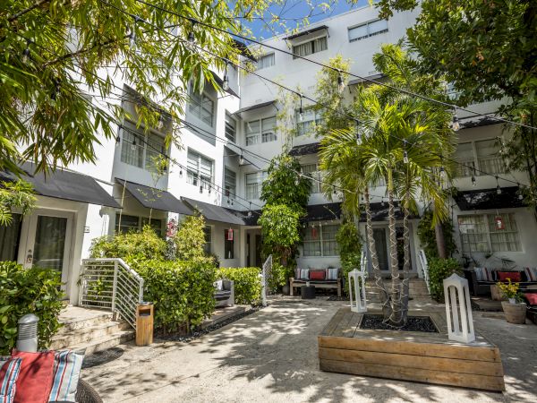 A sunny courtyard in a modern apartment complex with white buildings, green plants, and seating areas, under bright skies.