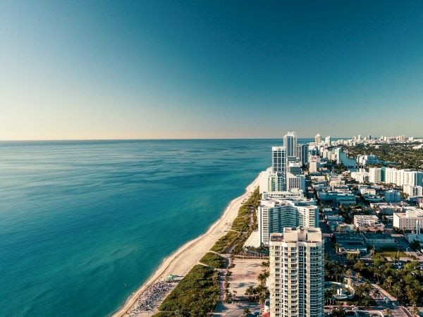 Aerial view of a coastal city: skyscrapers by the ocean and a long sandy beach under a blue sky.