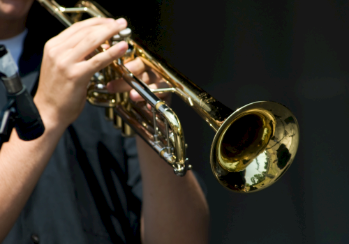 A musician is playing a shiny gold trombone on a dark stage.