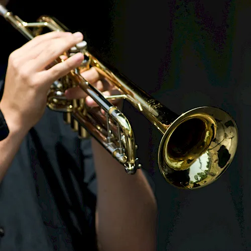 A musician is playing a shiny gold trombone on a dark stage.