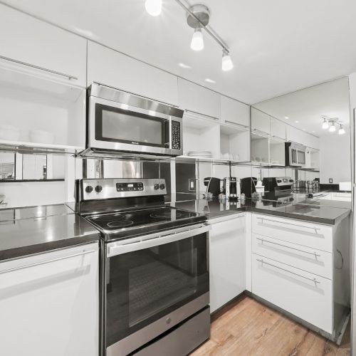 A modern commercial kitchen with a stainless oven and stovetop, microwave, white cabinets, and overhead lights.